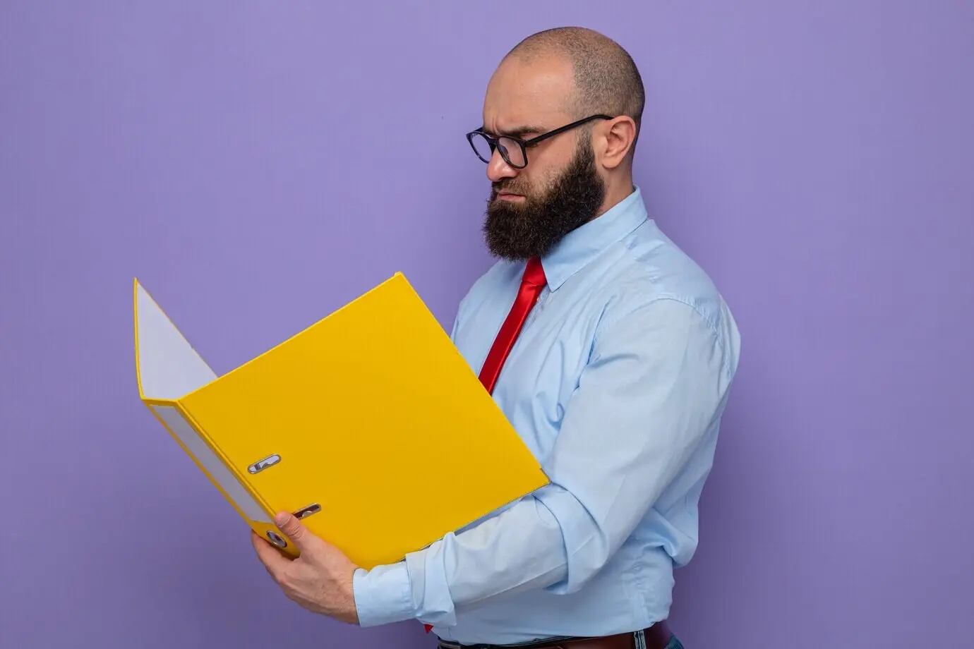 Ein bärtiger Mann mit Brille, roter Krawatte und blauem Hemd hält eine Büromappe und schaut sie mit ernstem Gesicht an.